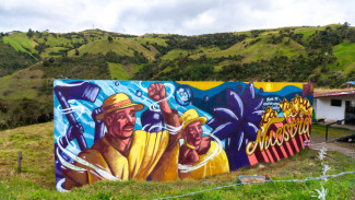 A colorful mural depicts two people wearing hats. The mural stands on a verdant landscape.