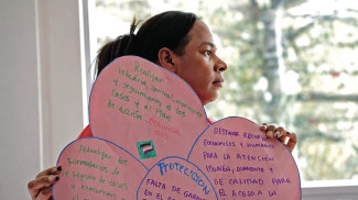A person holds up a poater collage made up of pink paper with text in Spanish